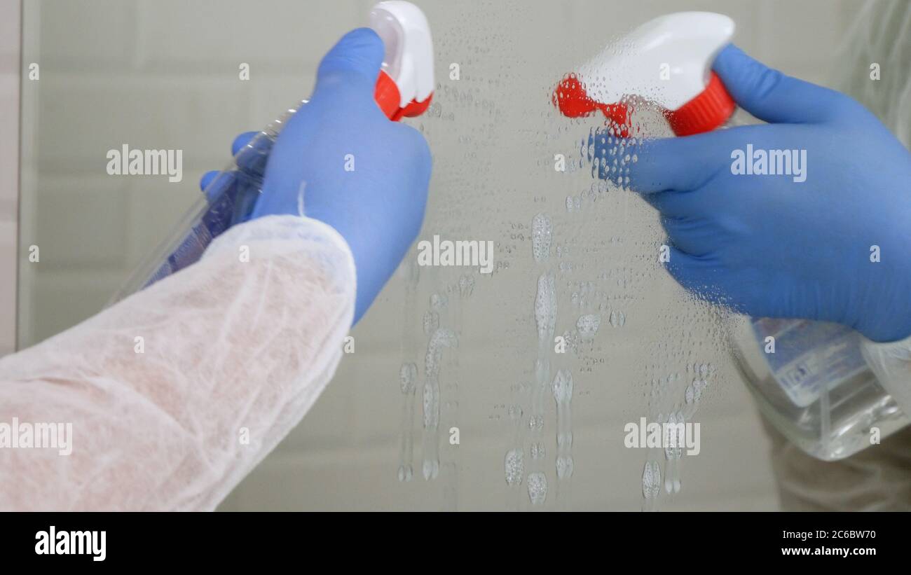 Person Wearing Protection Clothes Disinfecting a Mirror in a Bathroom