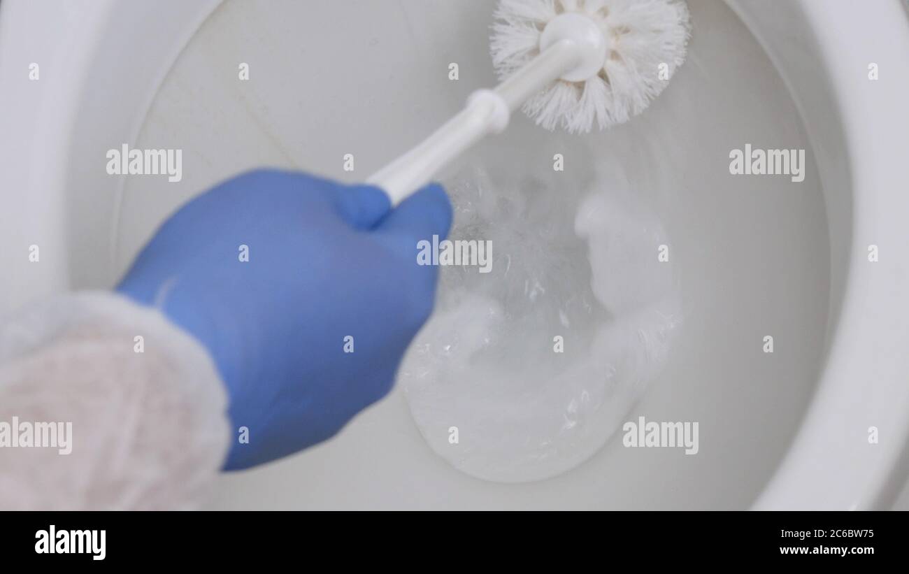 A Person with Protection Clothes and Gloves in Hands Disinfecting Toilet Bowl in Bathroom Using a Toilet Brush Stock Photo