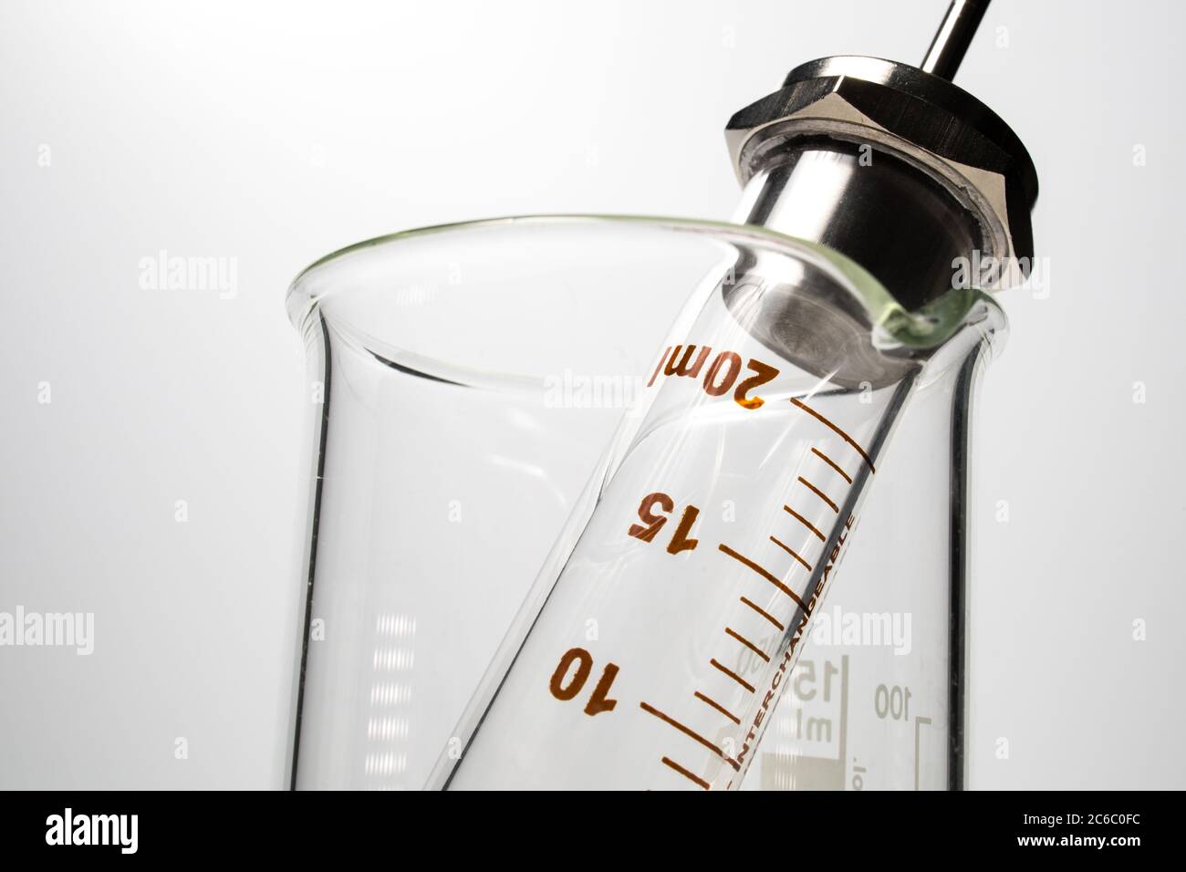 Closeup of a glass syringe in a glass beaker on a white background ...