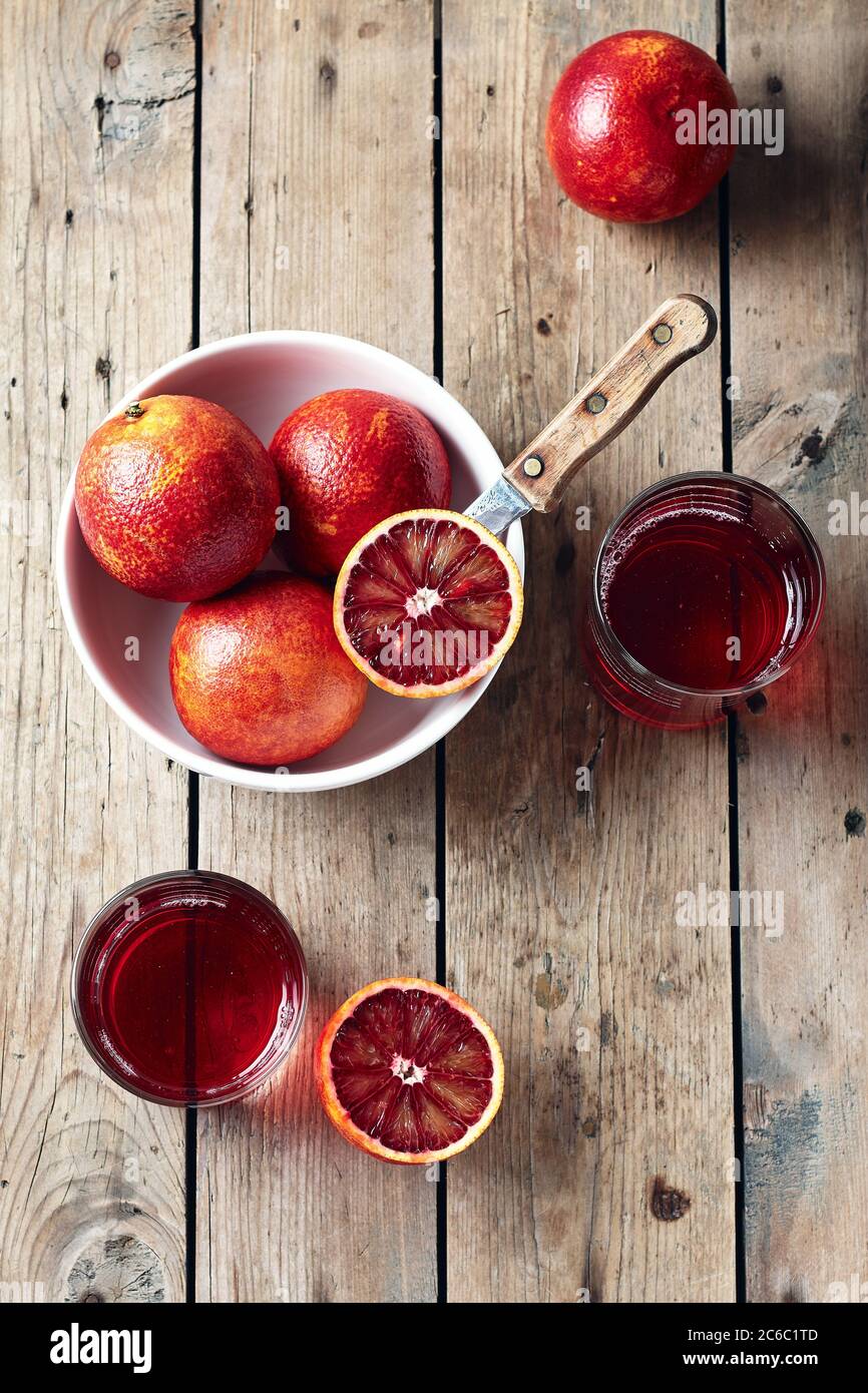 Red blood oranges in bowl and citrus drink on a wooden background, top view. Stock Photo