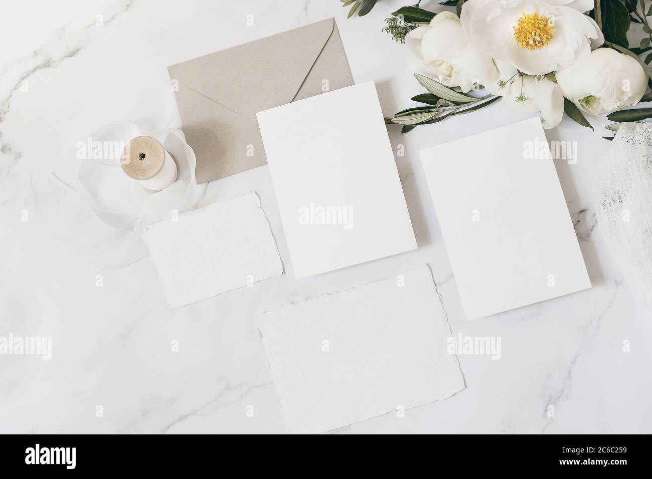 Wedding stationery, still life composition. Greeting cards mockup scene. Bouquet of white peony flowers, olive branches, cow parsley on marble table Stock Photo