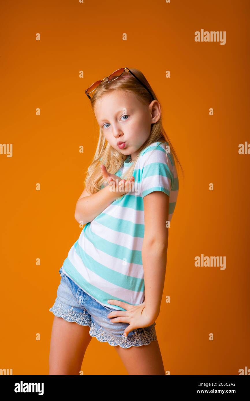 portrait of a happy blonde girl in a blue T-shirt on a yellow background. child's emotions, space for text Stock Photo