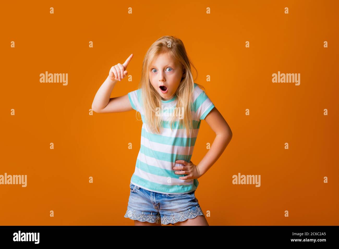 portrait of a happy blonde girl in a blue T-shirt on a yellow background. child's emotions, space for text Stock Photo