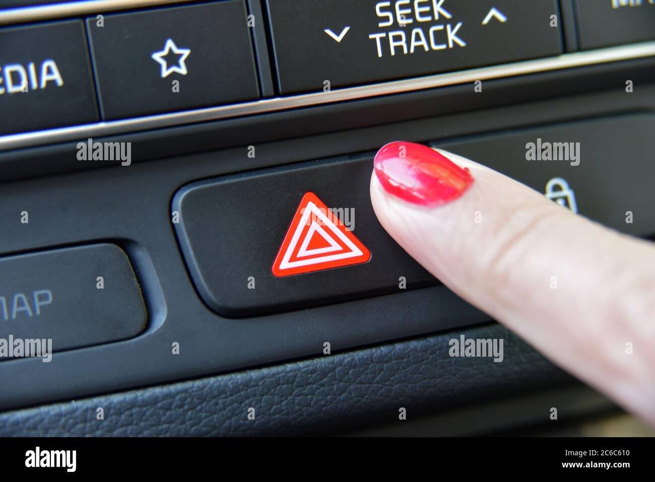 Woman pressing red triangle car hazard warning button. Female finger