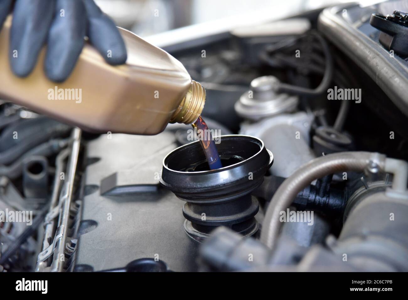 Adding Oil to a Car. Man's hand holding a bowl of motor oil and poured ...