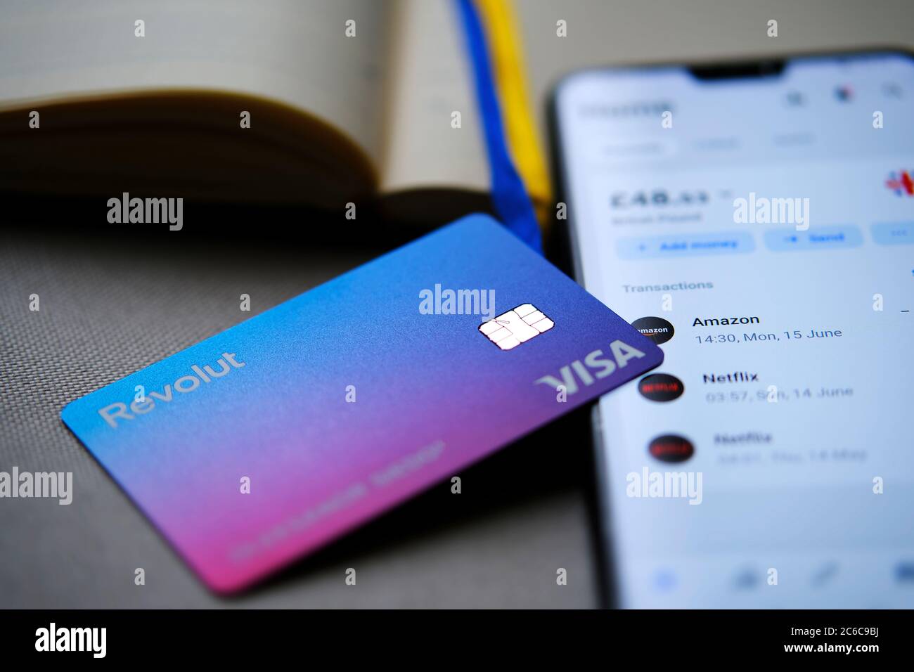 Stone / UK - July 8 2020: New redesigned Revolut Bank card placed on top of smartphone with Revolut app showing the balance on the screen. Selective f Stock Photo