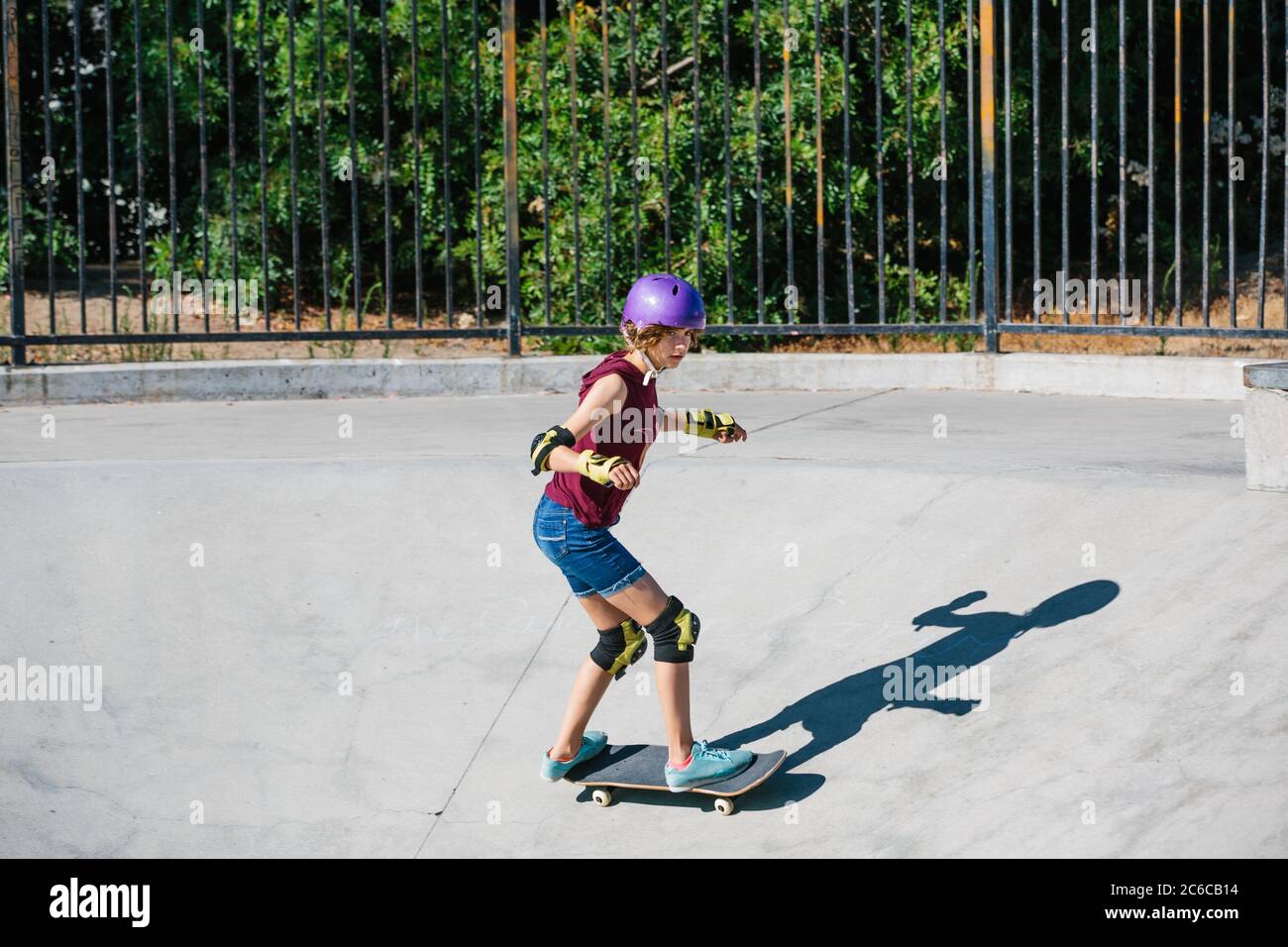 Teen girl in a purple helmet skateboards down a canyon at skate park Stock Photo