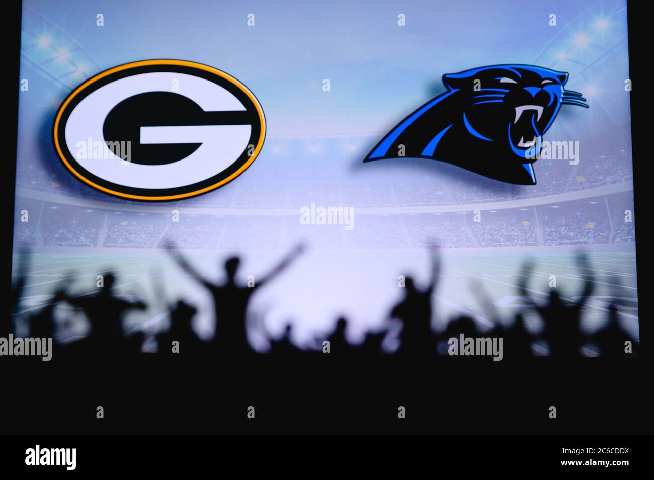 Green Bay Packers vs. Carolina Panthers. Fans support on NFL Game. Silhouette of supporters, big screen with two rivals in background. Stock Photo