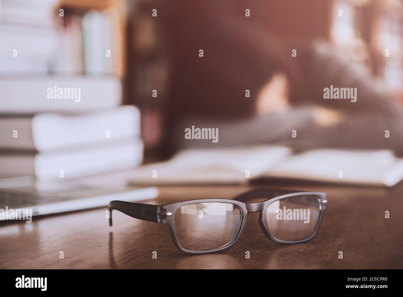 blur Close-shot of a glasses, young girl sleeping near a pile of books and laptop in the background. Stock Photo