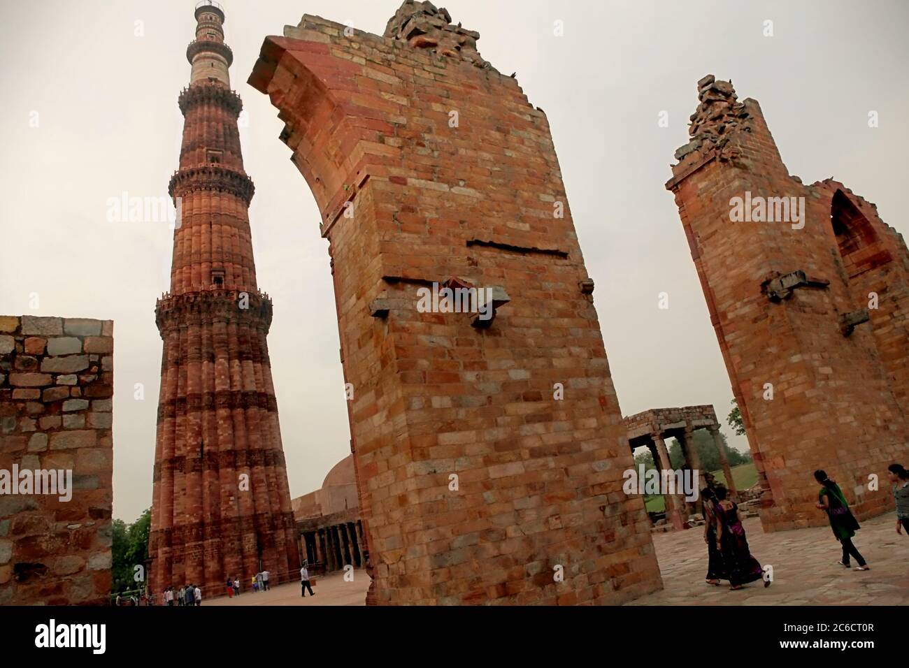 Tourists walking through the remaining gateway of Quwat-ul-Islam mosque with Qutab Minar towering in the background. Mehrauli, Delhi, India. Stock Photo