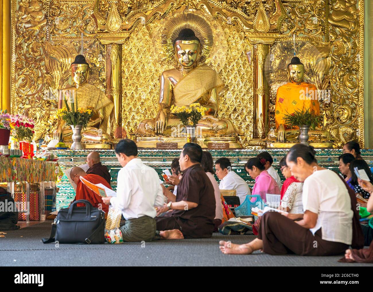Worshippers praying in front of gilded Buddha statues at the Shwedagon Pagoda in Yangon, Myanmar Stock Photo