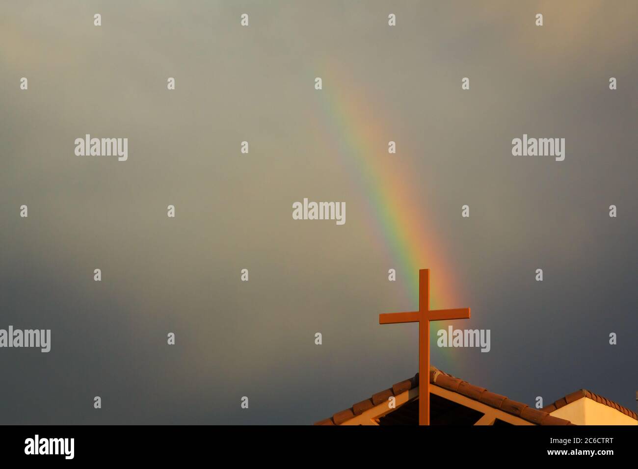 A passing storm creates a rainbow over a church cross. Stock Photo