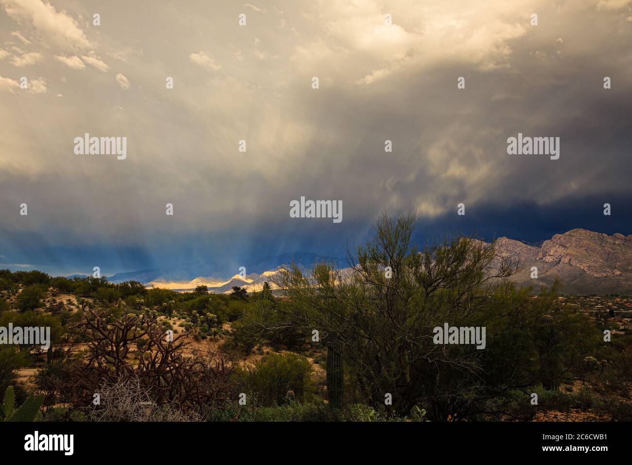 Rays of sunlight filter through the Winter clouds and illuminate the foothills of the Santa Catalina Mountains near Tucson, Arizona. Stock Photo
