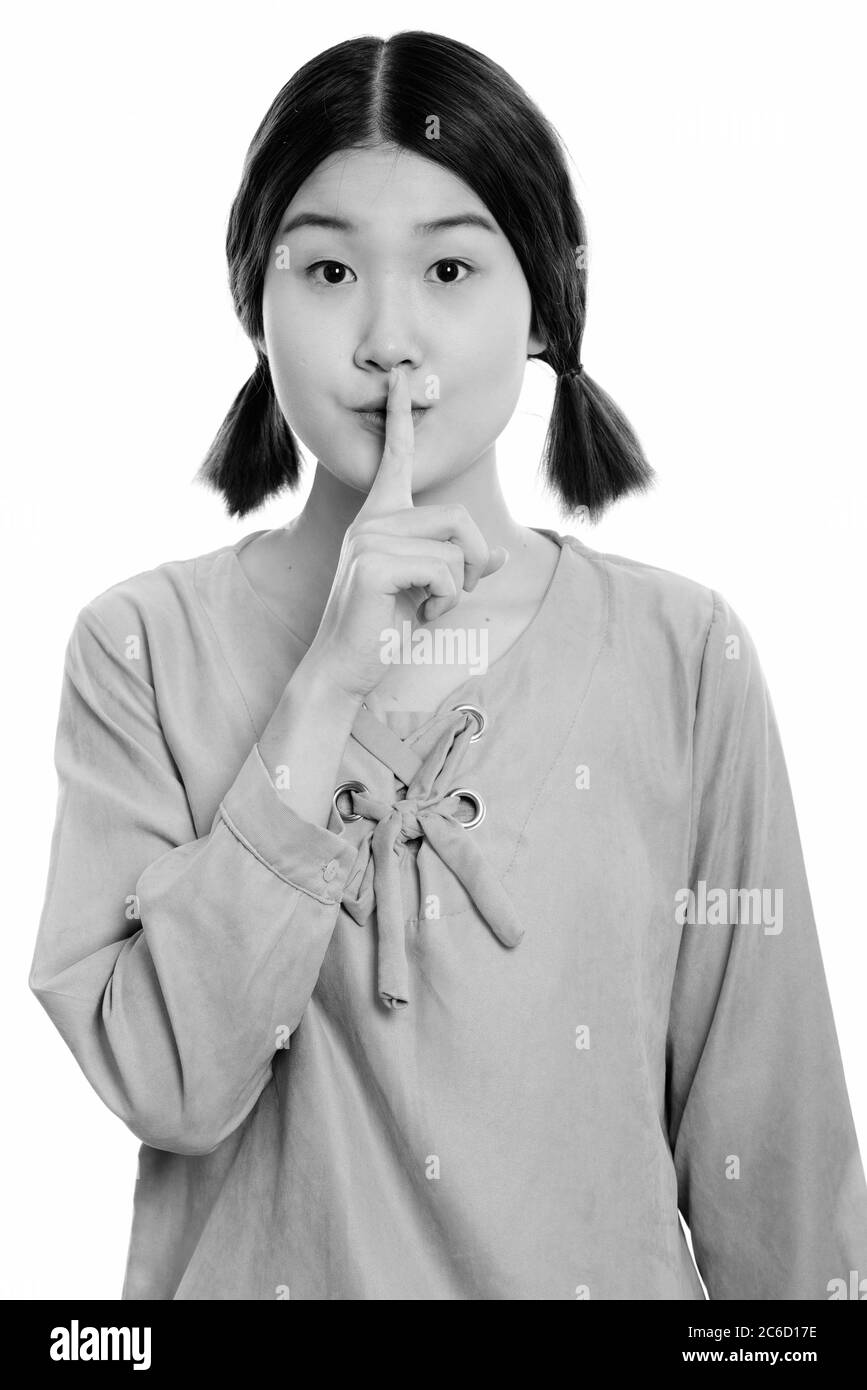 Studio shot of young beautiful Asian woman with finger on lips Stock Photo