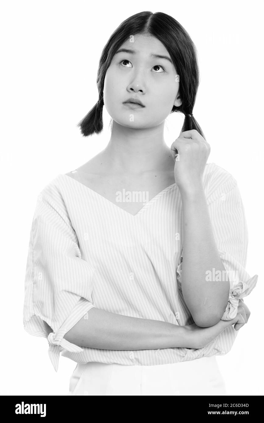 Studio shot of young beautiful Asian woman thinking while looking up ...