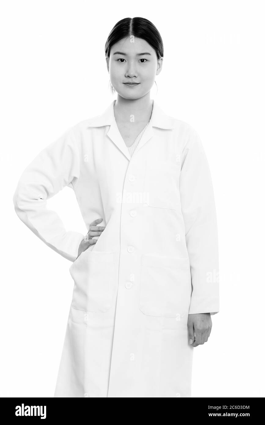 Studio shot of young beautiful Asian woman doctor standing with hand on ...