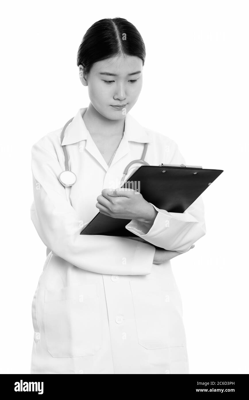 Studio shot of young beautiful Asian woman doctor reading on clipboard ...