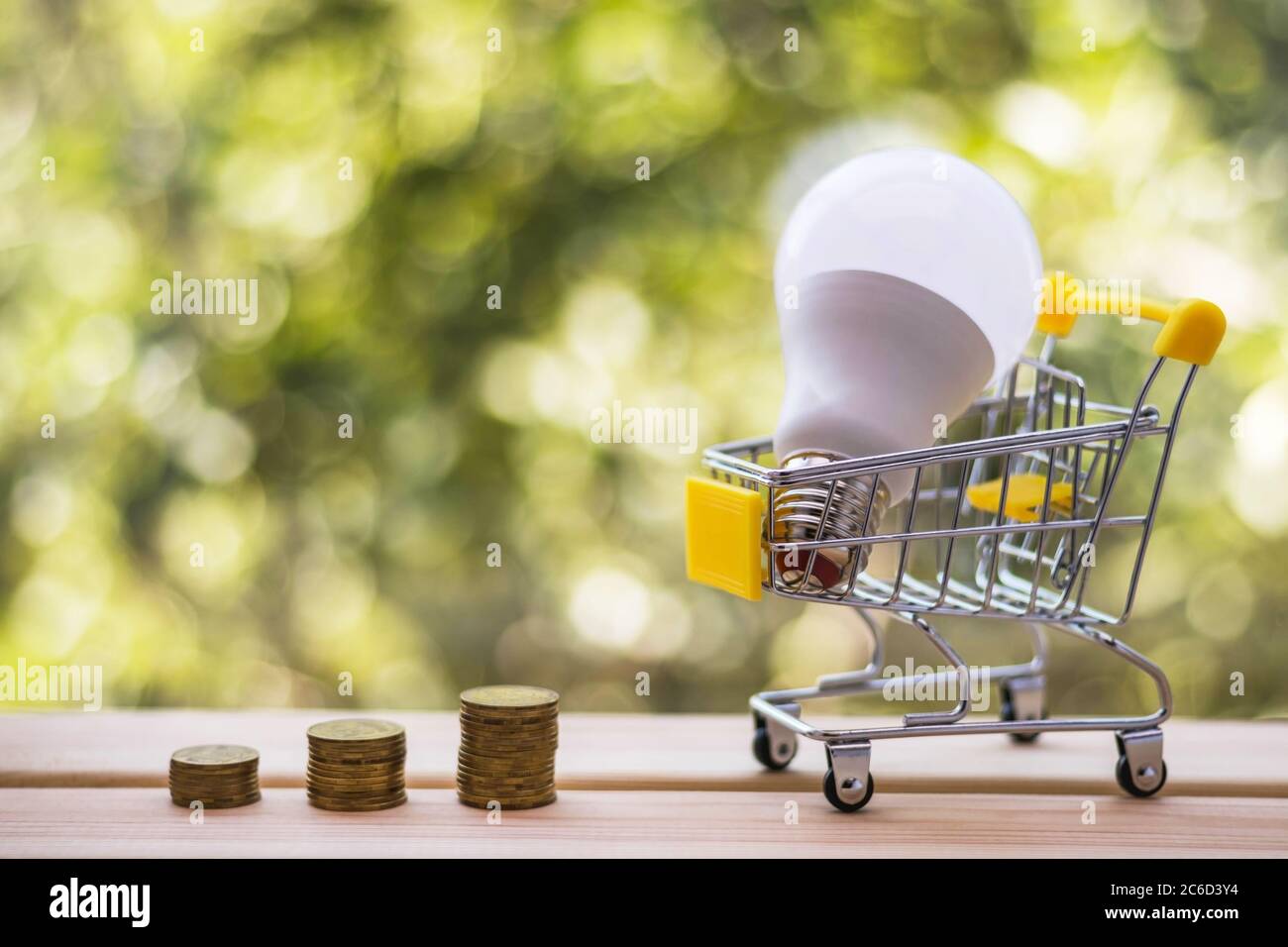 Stacks of coins and energy-efficient light bulb in mini shopping cart ...