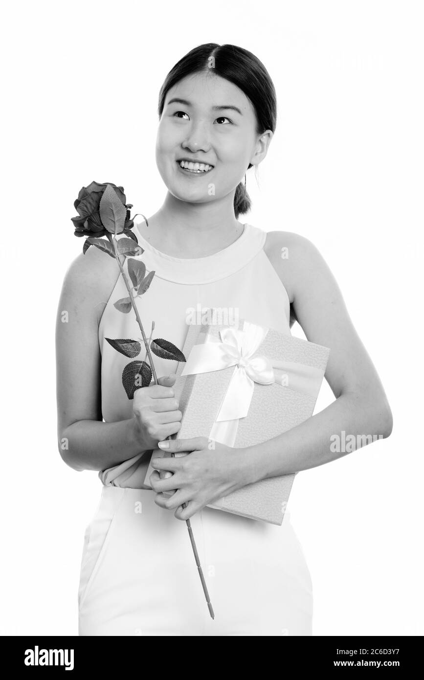 Young happy Asian woman smiling and thinking while holding red rose and ...