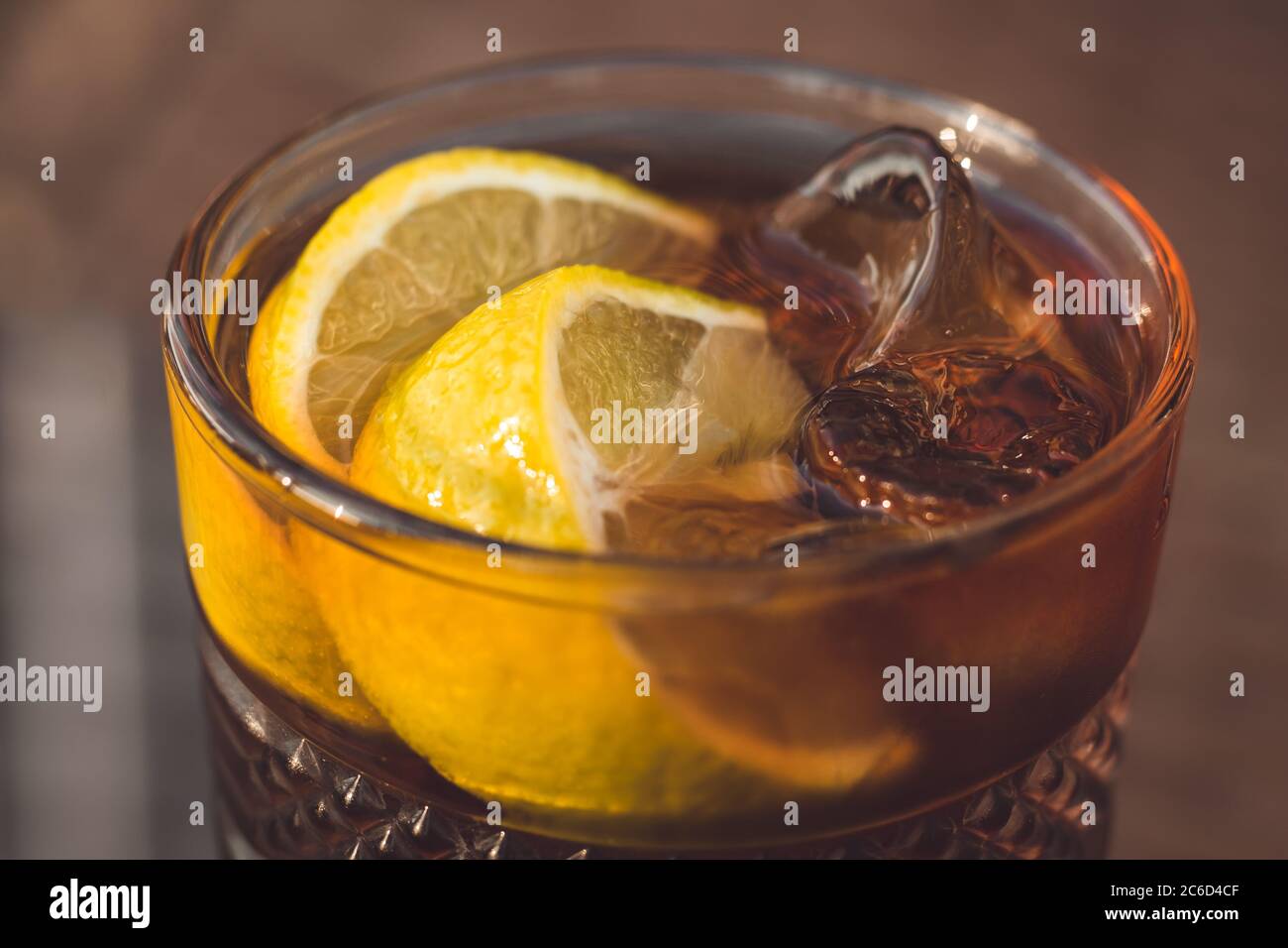 Glass of Long Island iced tea with lemon slice and straw. Close-up of an amber-colored alcoholic drink with ice on table in a bar, cafe Stock Photo