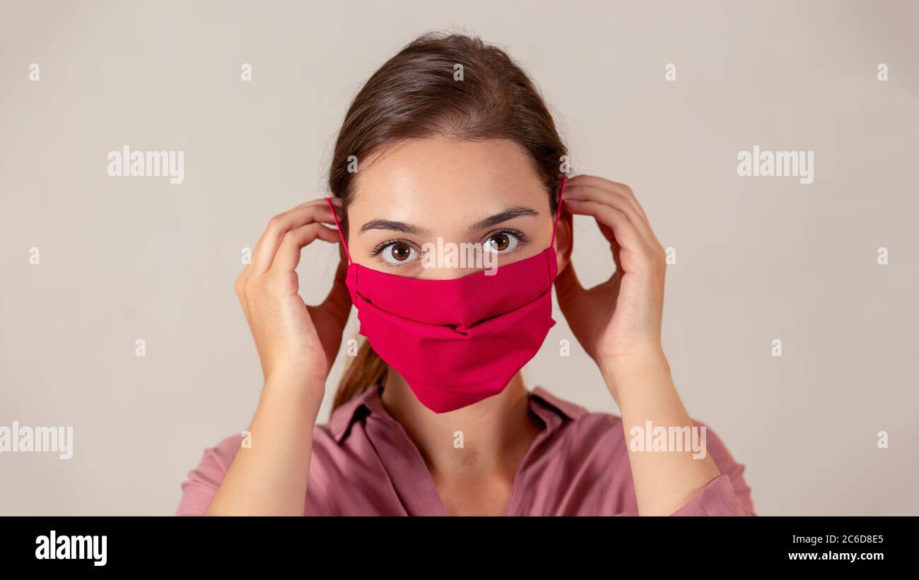 Young female nurse putting on a red fabric medical mask during pandemic. Stock Photo