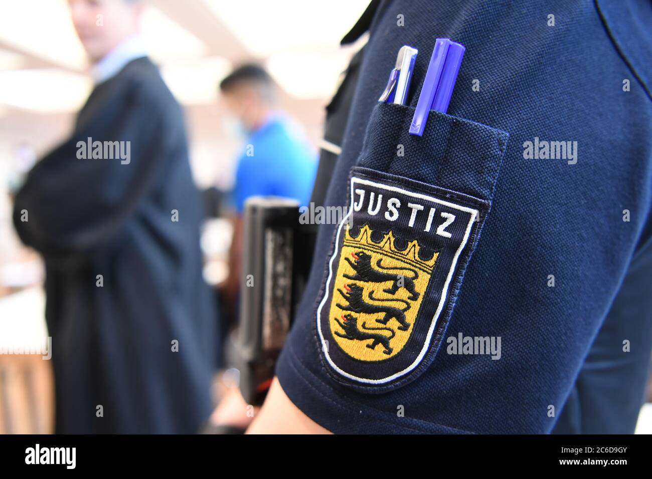 Ulm, Germany. 09th July, 2020. A defendant is standing in the courtroom at the Messe Ulm, while in the foreground is a member of the judiciary, whose judiciary logo can be seen. Five men are accused of raping a 14-year-old girl. Credit: Felix Kästle/dpa/Alamy Live News Stock Photo