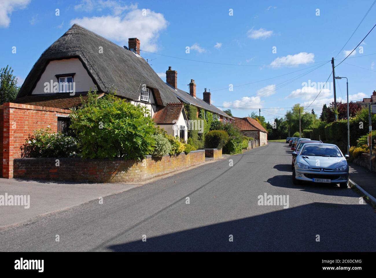 Thatched cottage, The Street, All Cannings, Wiltshire, England, with cars parked on one side of the road Stock Photo
