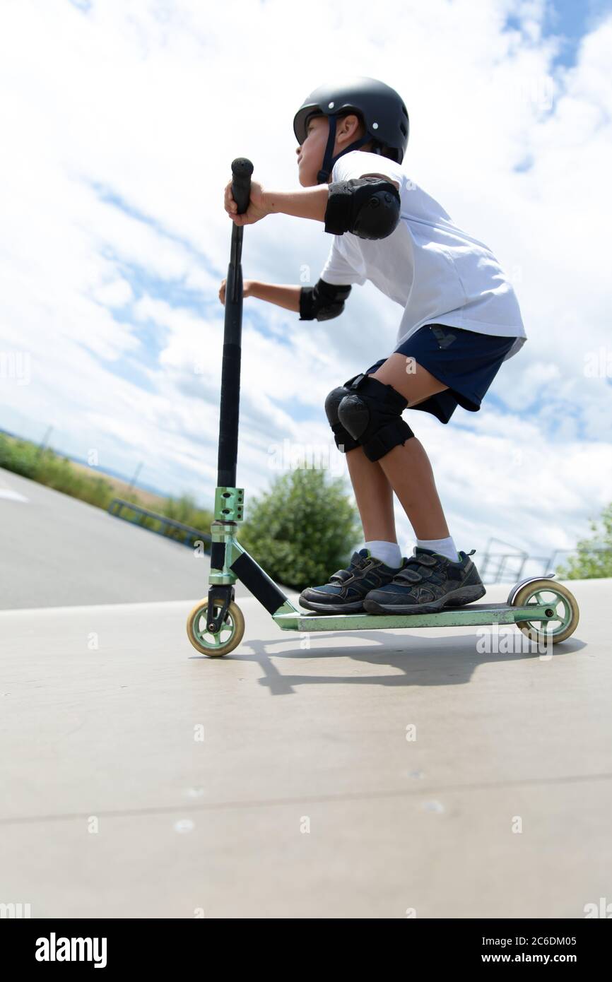 A cute little boy rides a scooter in a skatepark. A young novice athlete spends free time in extreme sports. Lifestyle. Stock Photo