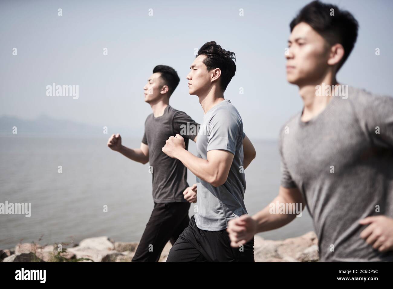 three young asian adult men running jogging outdoors by the sea Stock Photo
