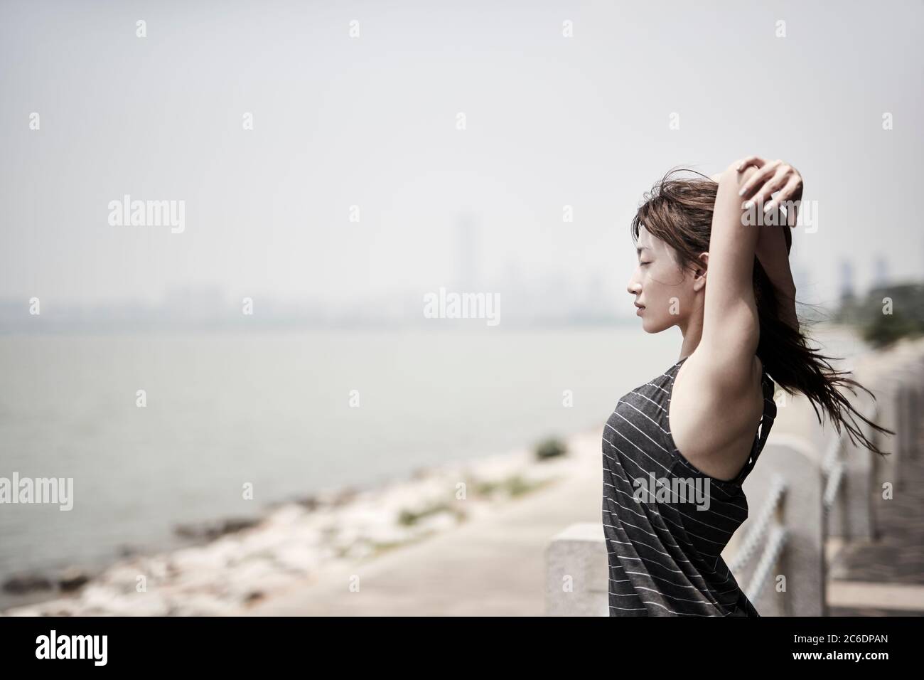 young asian adult woman stretching arms outdoors by the sea, side view Stock Photo