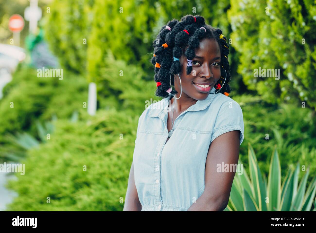 Portrait of a smiling young black woman in a park with sunlight flare ...