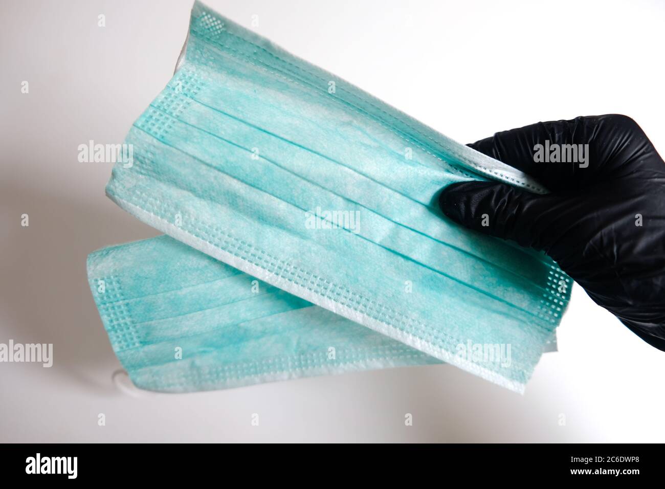 Hand in black glove holding a pair of face masks. Healthy measures to prevent virus spreading. Take the medical protection mask to flatten the curve Stock Photo