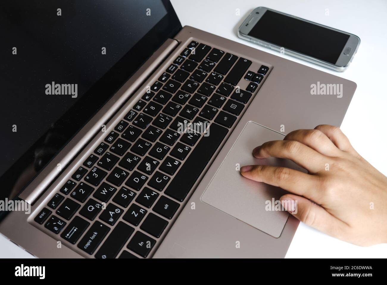 Two white female fingers using laptop touchpad gesture. Modern home office workspace. Using computer and smartphone for working and studying Stock Photo