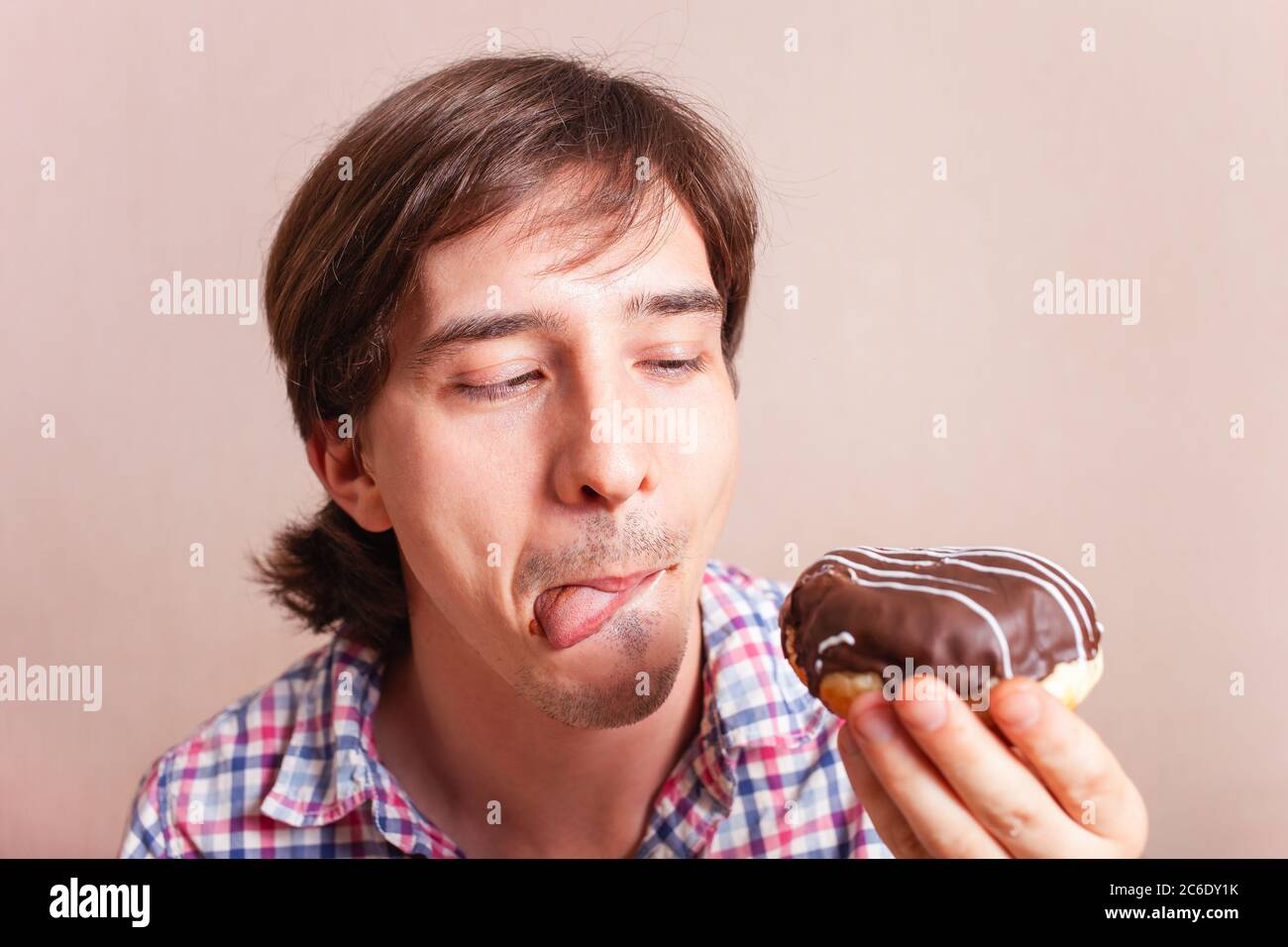 A man eats a doughnut and licks, a very funny photo on a pink background. Empty space for text. A man loves sweets chocolate. World Chocolate Day stoc Stock Photo