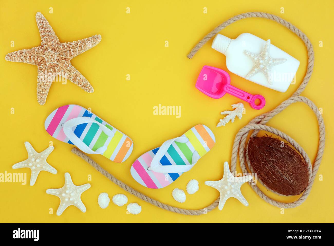 Summer holiday beach items with seashells, flip flops, coconut, rope and suntan protection lotion. Themed concept on yellow background with copy space Stock Photo