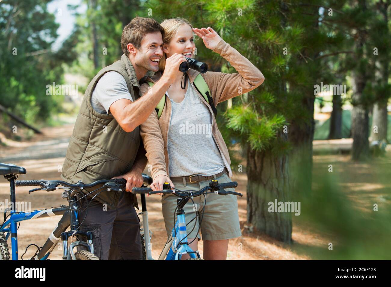Smiling couple with mountain bikes using binoculars in woods Stock Photo
