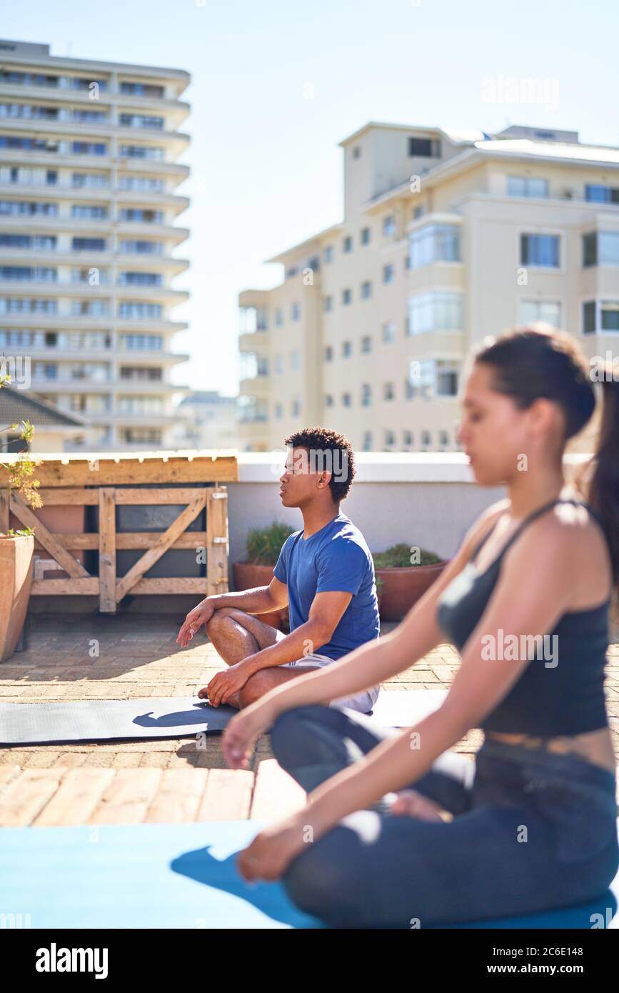 Young man and woman practicing yoga on sunny urban rooftop Stock Photo