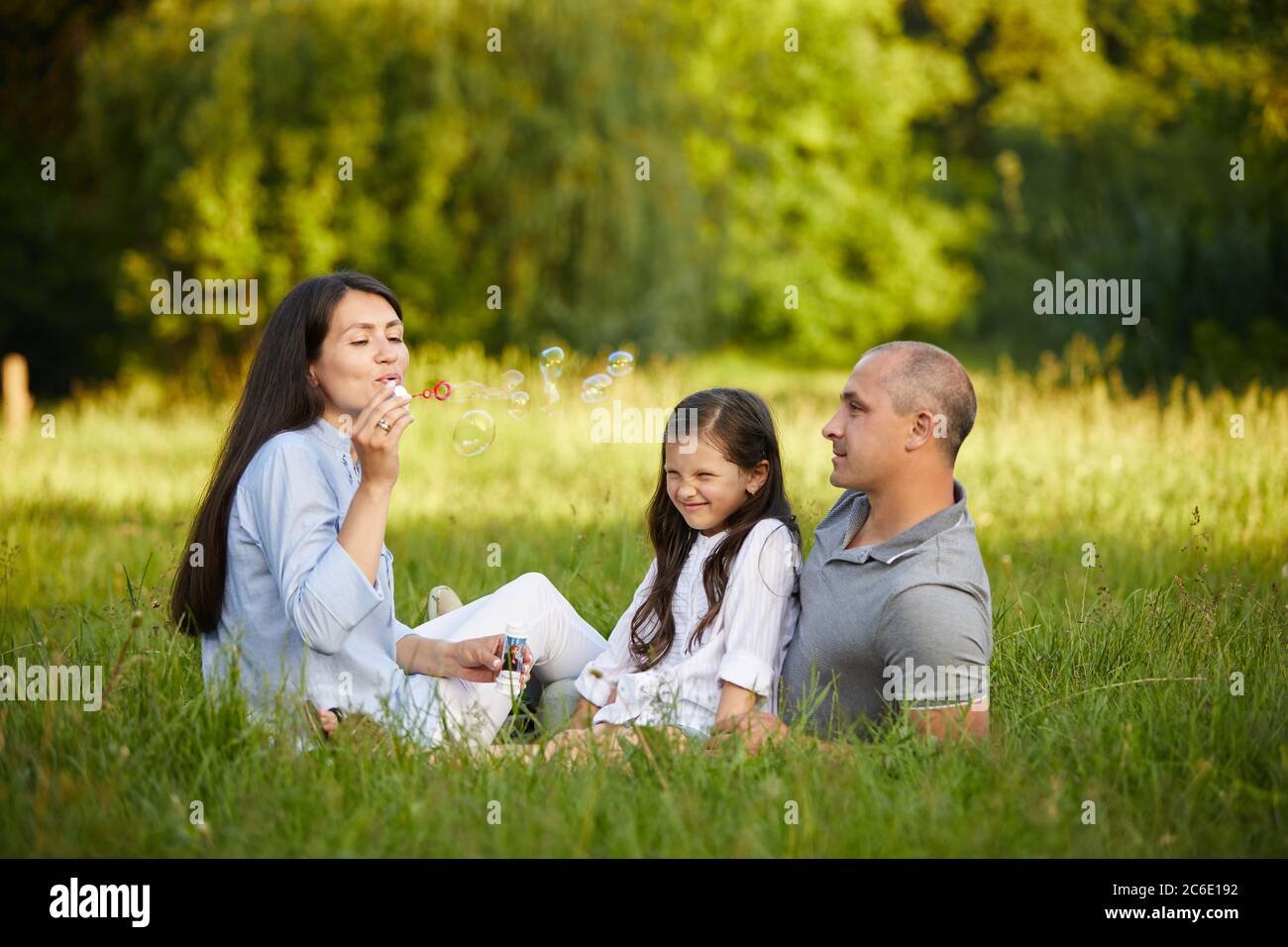 happy family with child girl blow soap bubbles together in park in ...
