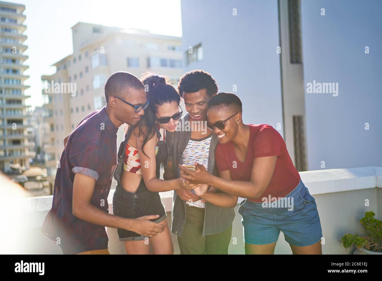 Young friends using smart phone on sunny rooftop balcony Stock Photo