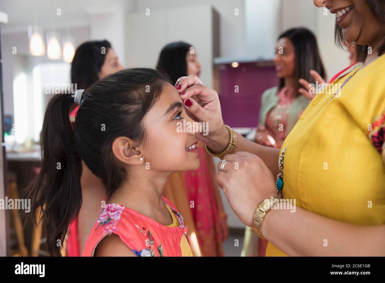 Indian mother placing bind on forehead of smiling daughter Stock Photo