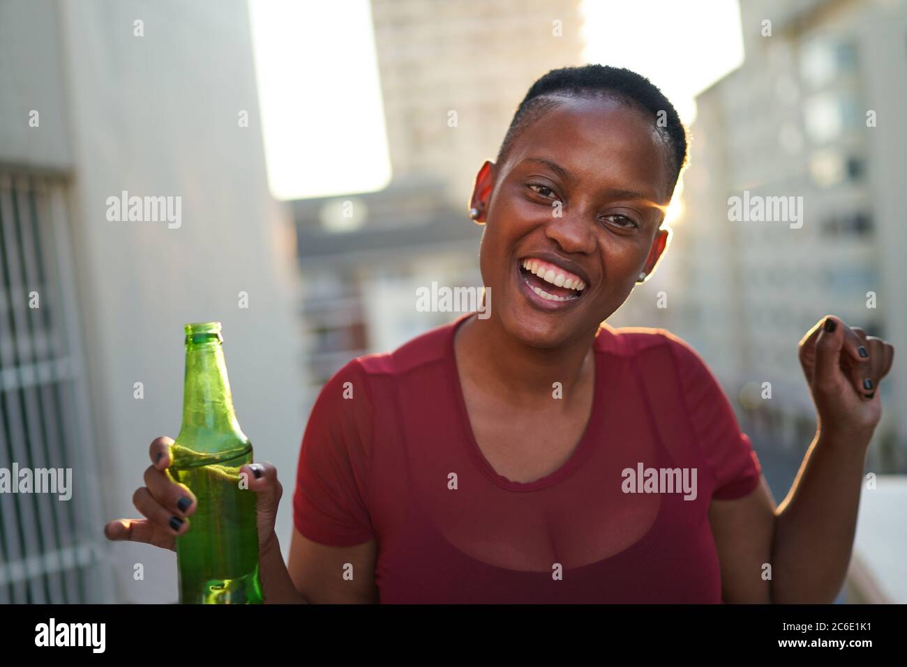 Portrait happy young woman drinking beer on urban balcony Stock Photo