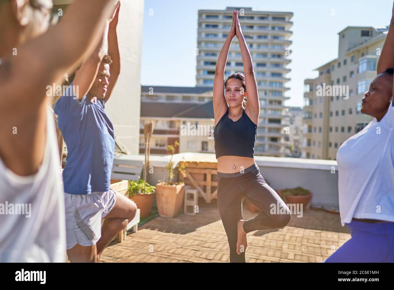 Young friends practicing yoga tree pose on sunny urban rooftop balcony Stock Photo