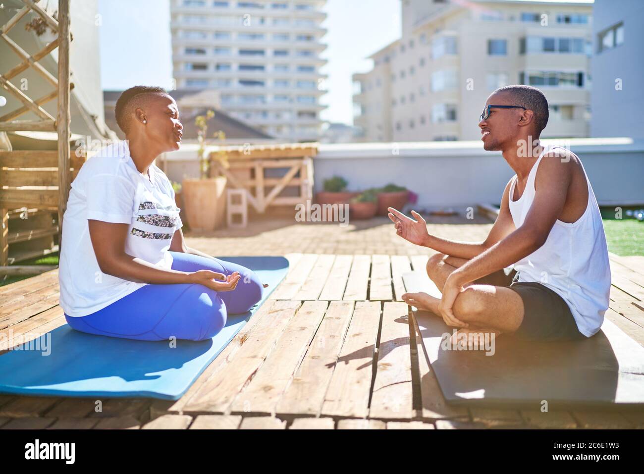 Young couple talking on yoga mats on sunny urban rooftop balcony Stock Photo