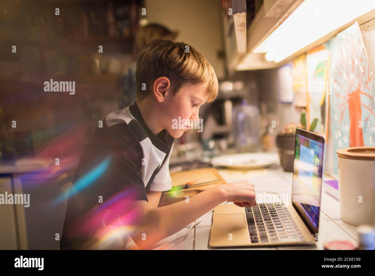 Focused boy doing homework at laptop in kitchen Stock Photo