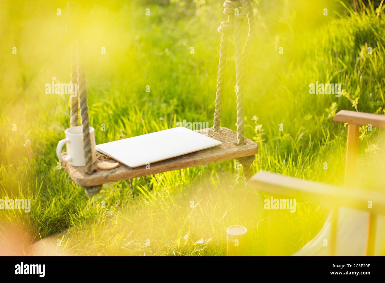 Laptop and coffee cup on swing in sunny garden Stock Photo