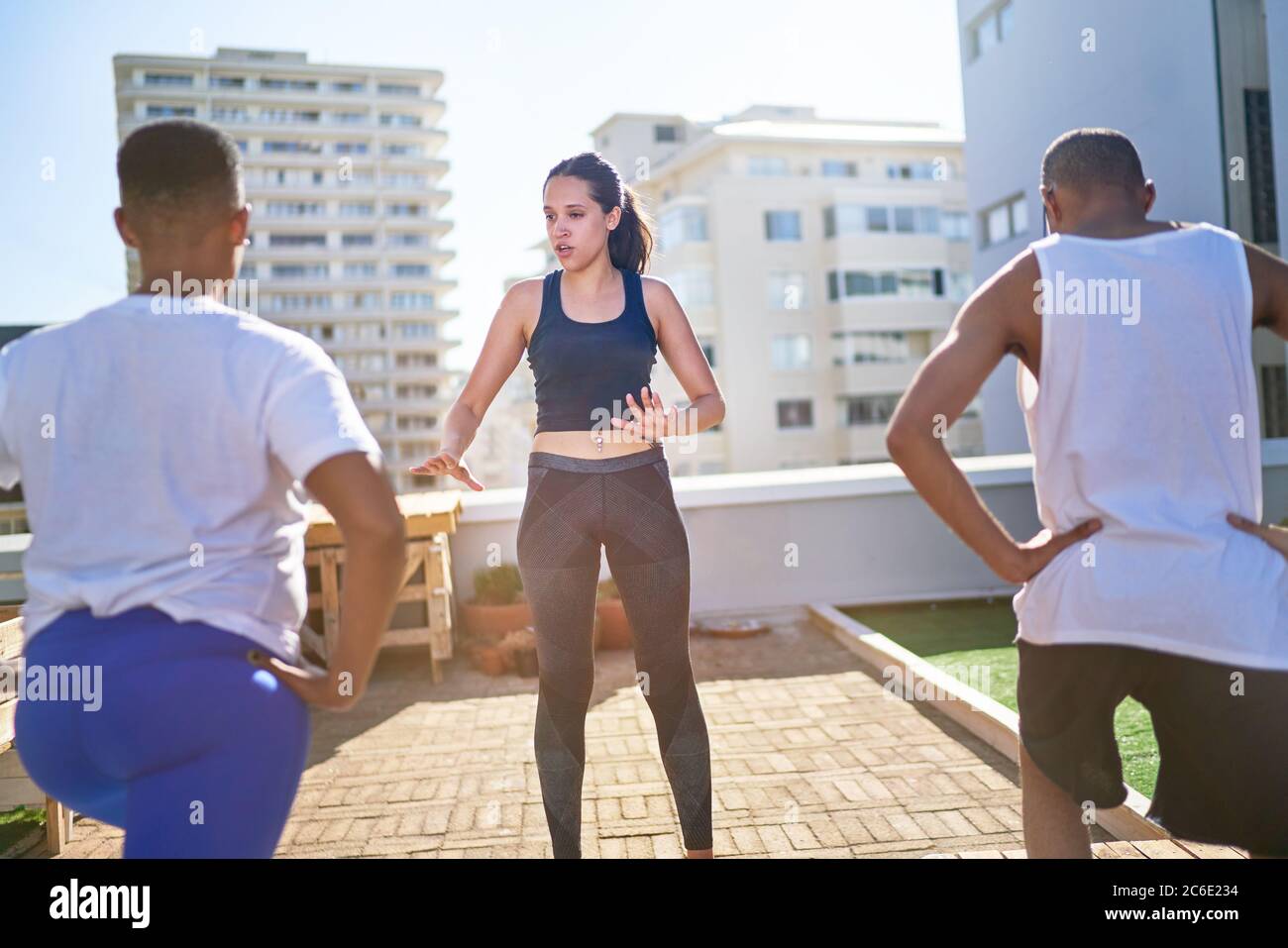 Young female yoga instructor teaching class on sunny urban rooftop Stock Photo