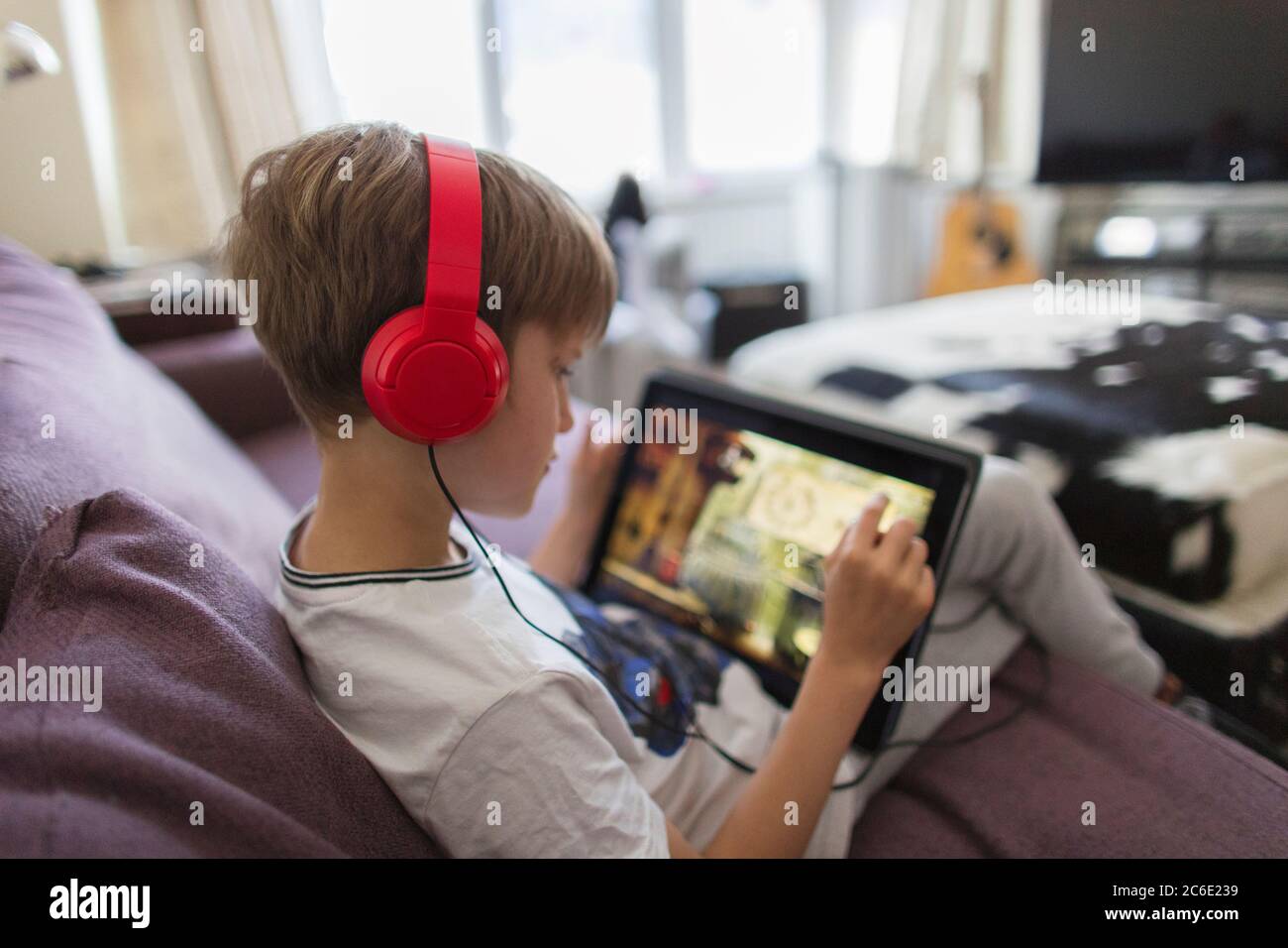 Boy with headphones and digital tablet playing video game on sofa Stock Photo