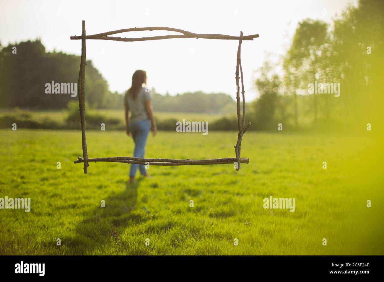 Branch frame over woman walking in idyllic sunny grass field Stock Photo