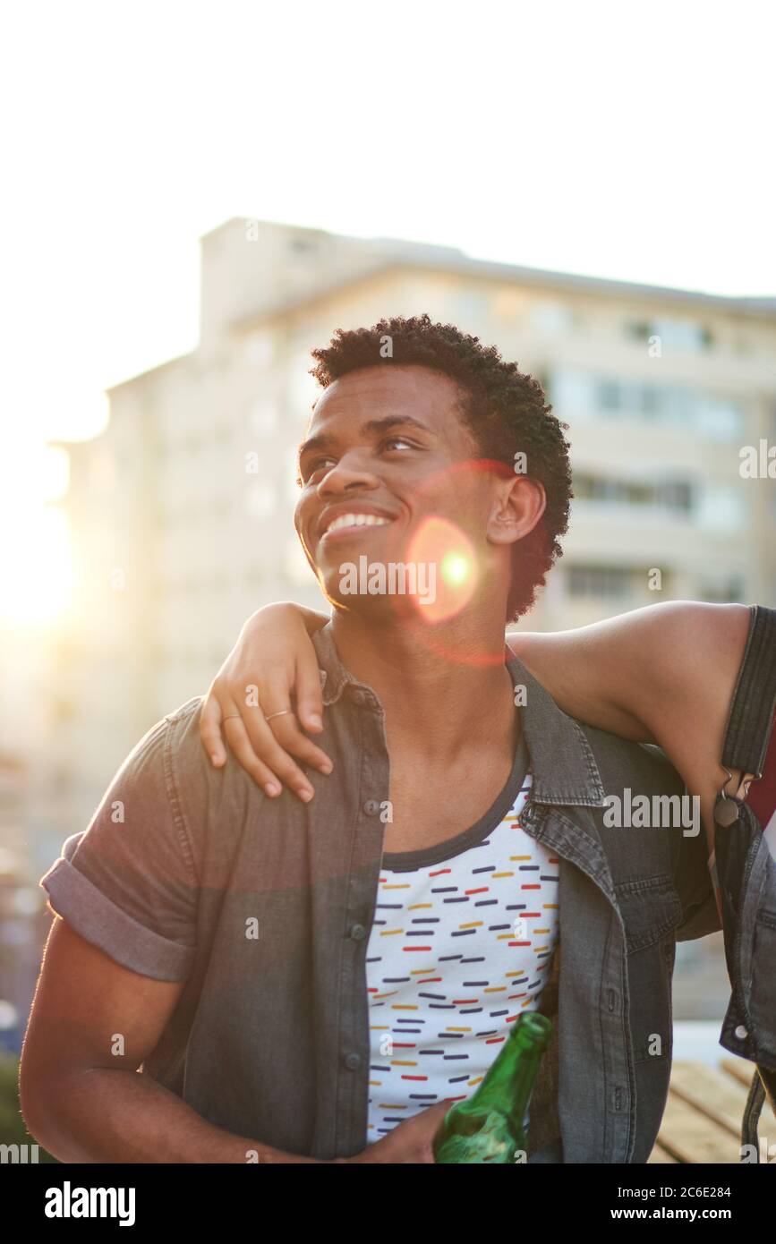 Happy young man drinking beer on sunny urban rooftop Stock Photo