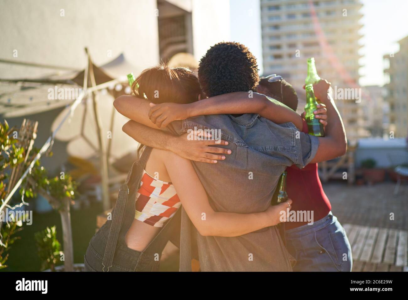 Happy young friends hugging and drinking beer on sunny rooftop Stock Photo
